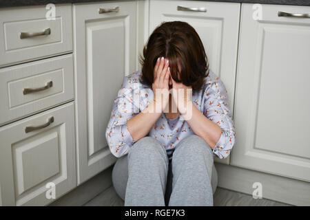 woman is sitting on kitchen floor covering her face with her hands. Depression, grief or frustration Stock Photo