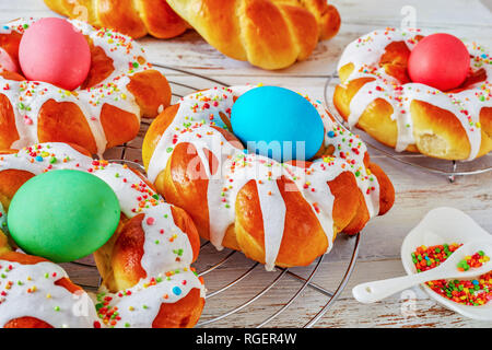 close-up of homemade sweet Italian Easter Bread Rings glazed around dyed egg and topped with colorful sprinkles on a wire rack, on an old white wooden Stock Photo