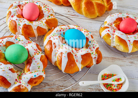 close-up of traditional sweet Italian Easter Bread Rings glazed around dyed egg and topped with colorful sprinkles on a wire rack, on an old white woo Stock Photo