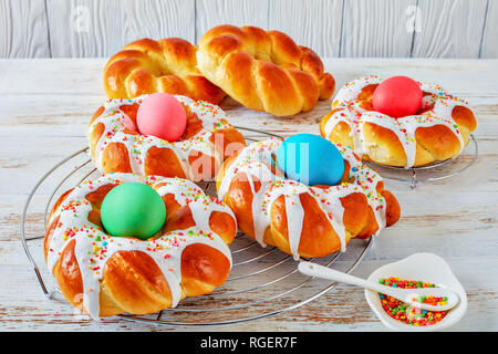 close-up of individual sweet Italian braided Easter Bread Rings glazed around dyed egg and topped with colorful sprinkles on a wire rack, on an old wh Stock Photo