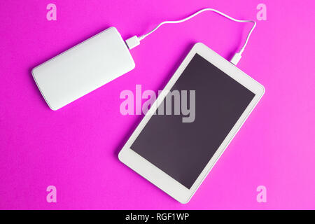 Flat lay of blank screen digital tablet device charging with power bank on pink background minimal creative concept. Space for copy. Stock Photo