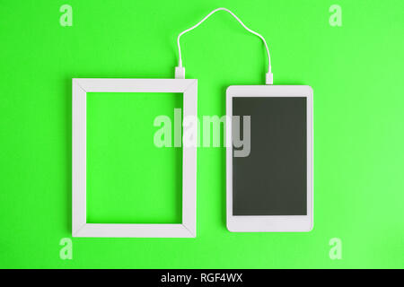 Flat lay of photo frame and blank screen digital tablet device connected with cable isolated on green background. Data transfer minimal creative conce Stock Photo