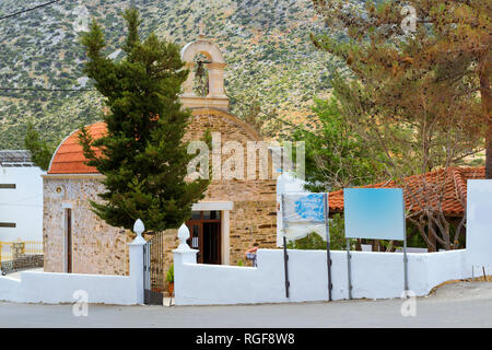 Eastern Orthodox Church, religious building made of stone with red tiled roof and bell in arch. Ekklisia Agia Triada. On background is mountains. Resort village Bali, Crete island Greece Stock Photo
