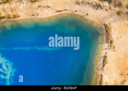 Abstract aerial image of a deep blue gravel lake in which sand is mined for the construction industry.
