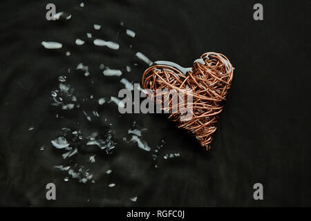 Copper wire heart made from reclaimed electric cable. Placed in water whose surface has been disturbed by droplets,