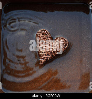 Heart made from copper wire in shallow water with concentric ripples caused by water droplets. Stock Photo