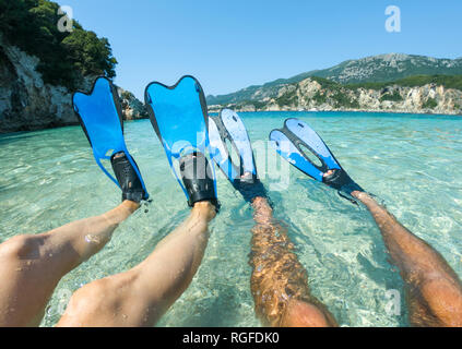 Blue snorkeling fins, flippers in crystal clear sea water. Snorkeler couple lie on the beach Stock Photo