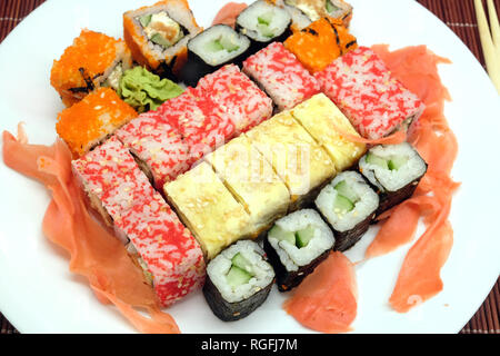 Sushi pieces on white plate and two chopsticks over brown wicker straw mat top view closeup Stock Photo