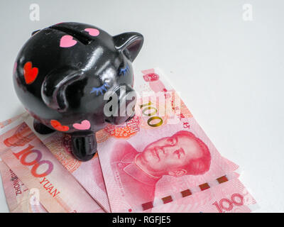 Black piggy bank standing next to Chinese 100 rmb banknotes on a white wooden background. The pig symbols fortune in the Chinese zodiac. Stock Photo