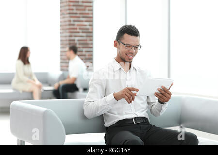 modern man uses a digital tablet sitting in the office lobby. Stock Photo