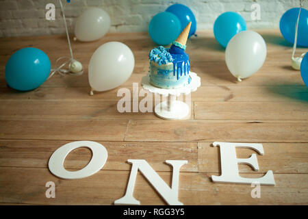 Decorations for one year birthday with a lot of blue and white balloons, festive cake and inscriptions on floor. Closeup. Stock Photo
