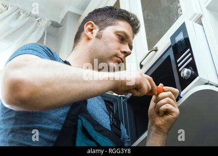 Male technician repairing microwave oven at home. Stock Photo