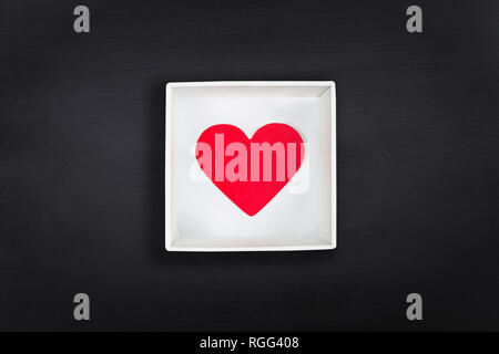 Red paper heart in white cardboard box on black chalkboard background. Flat lay Stock Photo