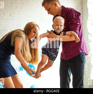 Parents wipe their one year old son who is stained with cake after celebrating his first birthday. Stock Photo