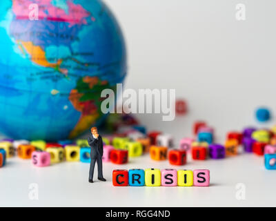 miniature figure businessman in dark blue suit standing backside of colorful of CRISIS alphabet and globe in the background and thinking of the crisis Stock Photo