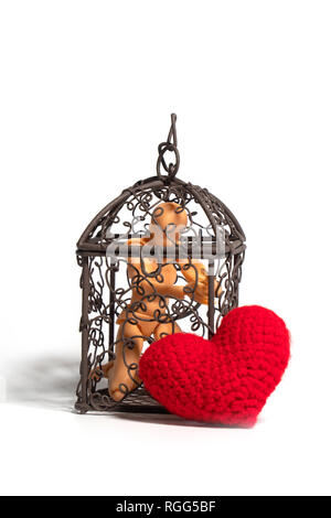 Action figure sitting in cage and there is a red heart on the outside on white background. Concept of Love, imprisonment and deprivation Stock Photo