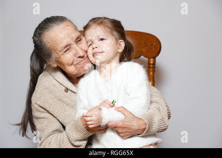 Сute gray long haired grandmother in knitted sweater hugs granddaughter with chicken pox, white dots, blisters on face. Concept family photo session,  Stock Photo