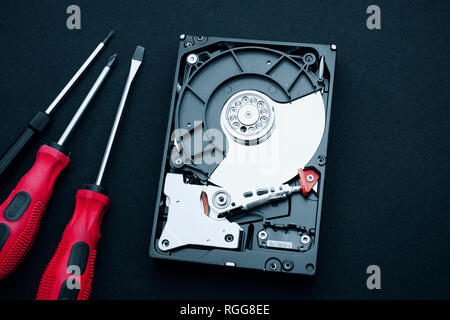 Top view of uncovered hard drive and screwdrivers on the desk. Hardware assembly inside showing magnetic platters discs and actuator read/write arm. Stock Photo