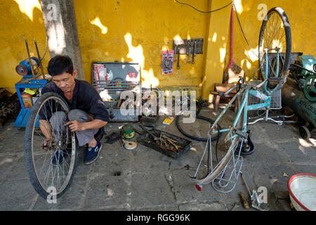 Asian mechanic repairing a bicycle on a street sidewalk Stock Photo