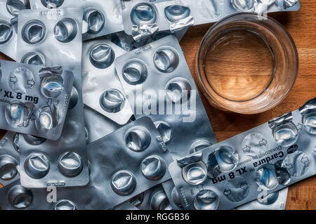 Empty used blister packs of tablets used to control high blood pressure on a bedside table with a glass of water. Medical shortage concept. Stock Photo