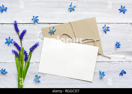 blank white greeting card and envelope with spring flowers bouquet on white wooden table. mock up. top view. spring concept Stock Photo