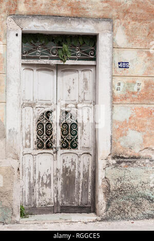Abandoned Doorway in Merida: A once white door seems abandones with plants breaking through the skylight window, rust on the decorative lattice and a large padlock and chain. Stock Photo