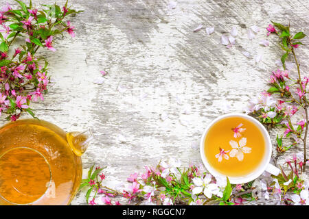 cup of green tea and teapot with branches of blossoming sakura and cherry on white rustic wooden background. flower spring tea. top view with copy spa Stock Photo
