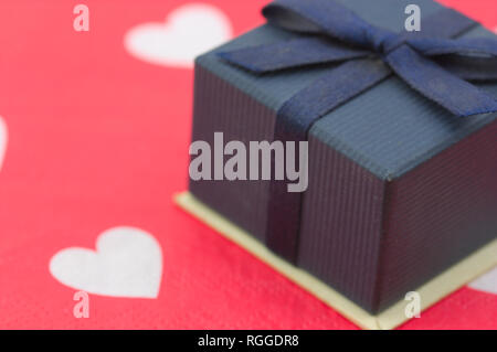 close-up of a blue gift box with lazito, on the table we have a paper decorated with white hearts on red Stock Photo