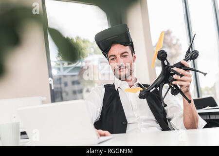 Businessman sitting in office working on a drone, using VR glasses Stock Photo