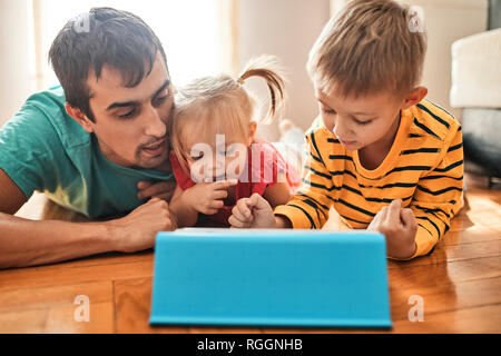 Father and his children lying on the floor at home using digital tablet Stock Photo