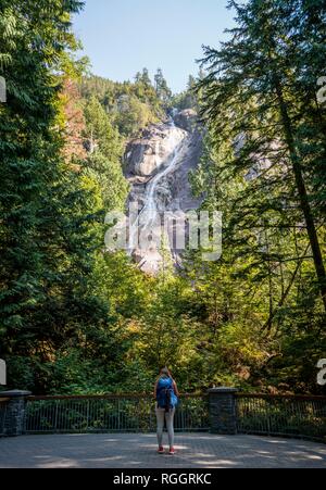 Young woman standing in front of Shannon Falls, waterfall on steep rock, British Columbia, Canada Stock Photo