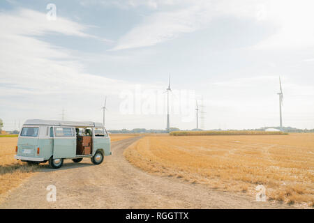 Camper van parked on dirt track in rural landscape with wind turbines