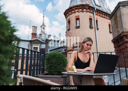Young woman sitting on roof terrace using laptop Stock Photo