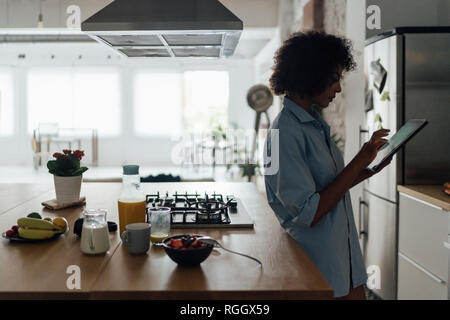 Woman standing in her kitchen, using digital tablet Stock Photo