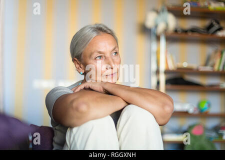 Portrait of pensive senior woman sitting on the couch at home Stock Photo