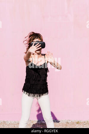 Young woman wearing VR glasses in front of pink wall Stock Photo