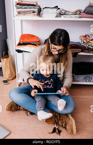 Mother and little daughter sitting on the floor at home using tablet Stock Photo