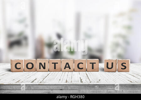 Contact us sign on a wooden desk in a bright living room with green plants Stock Photo