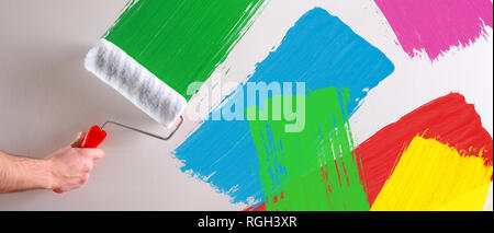 Man's hand painting multicolored  samples with roller on a white wall. Horizontal composition. Stock Photo