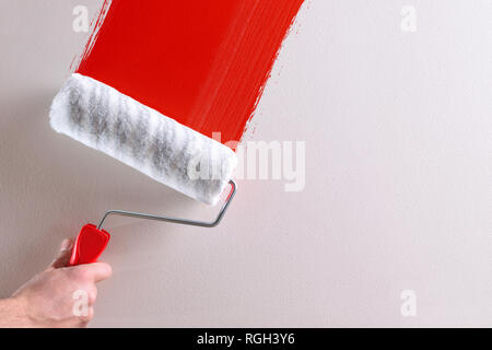 Man's hand painting a red sample with roller on a white wall. Horizontal composition. Stock Photo