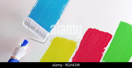 Professional painter's hand painting multicolored samples with roller on a white wall. Horizontal composition. Stock Photo