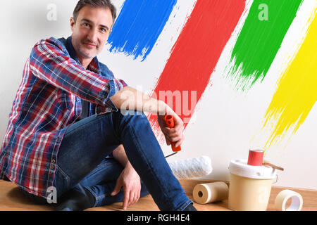 Man sitting on a parquet floor prepared with paint material to repaint his house and wall painted with colors close up. Front view. Horizontal composi Stock Photo