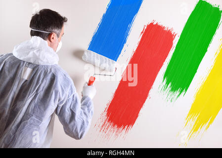 Background with professional painter with working overalls and roller on the back of a white wall painted with four colors. Horizontal composition. Stock Photo