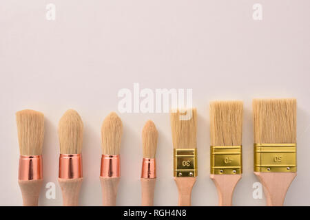 Set of paintbrushes for house painter of various sizes and shapes aligned on white table. Horizontal composition