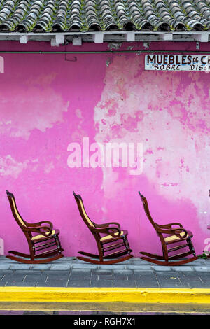 Traditional Poltrona style wooden rocking chairs on display against a pink wall in Tlacotalpan, Veracruz, Mexico. The tiny town is painted a riot of colors and home to legendary Mexican musician Agustín Lara. Stock Photo