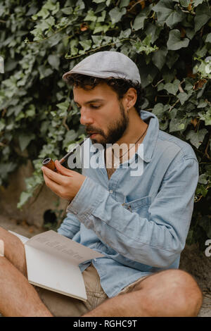 Young man smoking pipe, reading a book Stock Photo