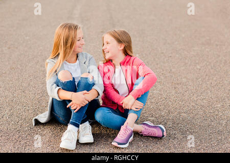 Two smiling girls sitting side by side on the ground Stock Photo