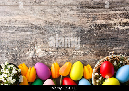 Colorful easter eggs in a basket and tulips on wooden table. Top view. Copyspace Stock Photo