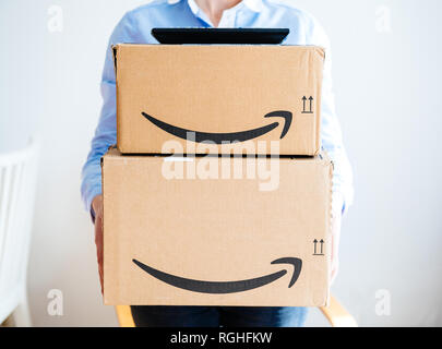 PARIS, FRANCE - MAR 16, 2018: Vie from the front of happy smiling woman holding two large Amazon Prime cardboard boxing after delivery - TV set remote on top on boxes  Stock Photo