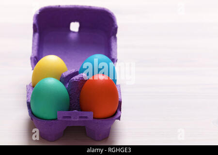 Easter composition. A set of four colorful eggs in a purple box on a white table. Copy space Stock Photo